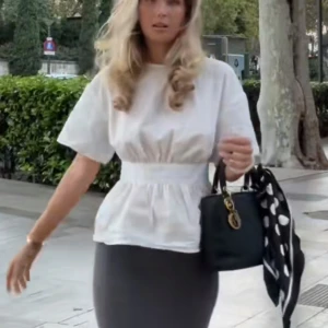 Vit blus med öppen rygg och knyt - Supersnygg vit blus med korta ärmar, markerad midja och volang nedtill. Baksidan har en djup öppen rygg med breda band som knyts i en rosett. Perfekt för dig som gillar trendiga detaljer och vill sticka ut lite extra.