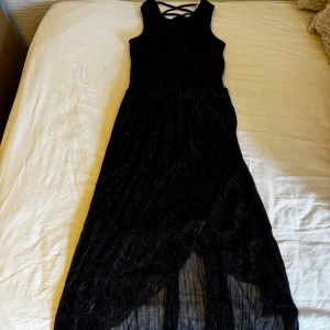 Svart blå-glittrig långklänning Lindex - Supersnygg svart långklänning från Lindex med glittriga detaljer och omlottkjol. Klänningen har ärmlös design och cool snörning i ryggen. Materialet är lätt och skimrande, perfekt för att sticka ut. Använd men i fint skick!                          Skickar ditt köp inom 24h!💘