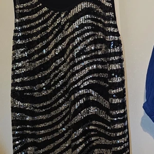 Svart paljettklänning Gina Tricot XL - Snygg svart kortklänning från Gina Tricot i storlek XL. Framsidan är täckt av glittriga paljetter i zebramönster med silver och svart, medan baksidan är helsvart. Ärmlös modell med rund halsringning, perfekt för att sticka ut.