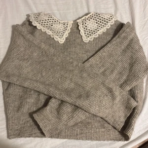 Beige stickad tröja med spetskrage - Superfin beige stickad tröja med lång ärm och en vit spetskrage som ger en söt vintagekänsla. Tröjan har ribbade muddar och är perfekt för lager-på-lager. Passar dig som gillar en mjuk och mysig stil med unika detaljer.