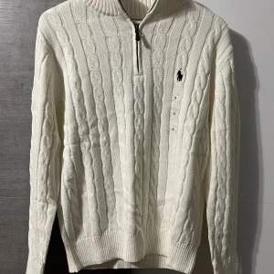 Polo Ralph Lauren half zip - Orginal pris: 2113kr, endast för 899kr hos Luxe Vibes! Kabelstickad vit tröja från Polo Ralph Lauren med halv dragkedja och broderad marinblå logga på bröstet. Tröjan har ribbad krage, ärmslut och nederkant. Perfekt för lager-på-lager och snygg till jeans eller chinos.