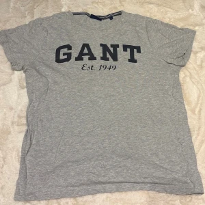 Grå GANT t-shirt med tryck - Grå t-shirt från GANT med stort svart tryck på bröstet där det står 'GANT Est. 1949'. Klassisk rund halsringning och korta ärmar.
