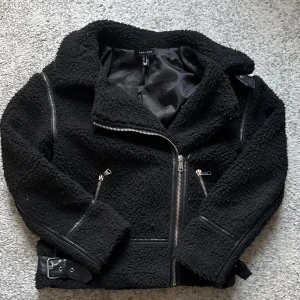 Svart teddyjacka från New Look - Svart teddyjacka från New Look med cool pilot stil, bälte detalj. Jackan har mjukt teddy-material och detaljer i skinnimitation längs sömmarna och vid bältet. 
