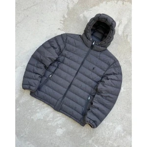 Grå dunjacka från Polo Ralph Lauren - Grå dunjacka från Polo Ralph Lauren med huva och dragkedja framtill. Jackan har ett quiltat mönster, två sidofickor med dragkedja och elastiska muddar vid ärmslut. Perfekt för kalla dagar och har en stilren look med diskret logga på bröstet. Storlek S. Pris kan diskuteras genom snabbaffär