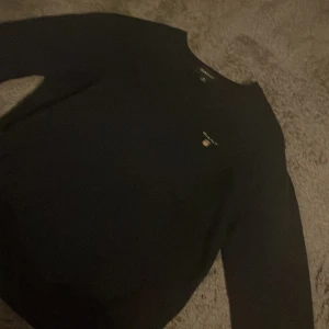 Mörkblå stickad tröja från GANT - Snygg mörkblå stickad tröja från GANT med logga broderad på bröstet. STOR I STORLEKEN!!!! Passar mig som har xxs!bra pris om man jämför med några andra likadana tröjor🤎