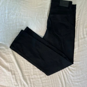 Svarta jeansbyxor från Cheap Monday - Svarta jeansbyxor från Cheap Monday i modellen Regular Stay Black. Klassisk femficksdesign med rak passform och svart läderpatch bak i midjan. Jeansen är tillverkade i ett slitstarkt bomullsmaterial med en snygg, djup svart färg.