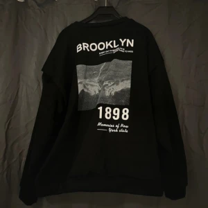 Svart oversized Brooklyn sweatshirt - Svart oversized sweatshirt med tryck på ryggen. Tröjan har rund halsringning och långa ärmar, perfekt för en chill streetstyle-look. Mysig och avslappnad. Knappt använd