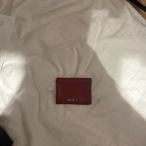 Röd kortplånbok från Hugo - Slimmad röd kortplånbok från Hugo i skinn med stilren design och silverfärgad logga framtill. Perfekt för kort och lite kontanter, smidig att ha i fickan. Klassisk och enkel look som passar till allt.