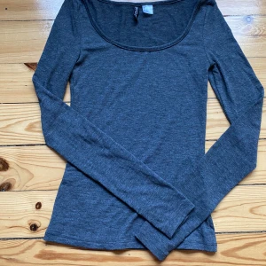 Mörkgrå långärmad topp från H&M - Säljer en stilren mörkgrå långärmad topp från H&M Divided i storlek XS. Toppen har en rundad, lite djupare halsringning och är gjord i mjuk bomullsmix som känns skön mot huden. Perfekt att matcha med jeans eller kjol för en enkel och snygg look.