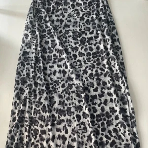 Leopardmönstrad långkjol i grått - Säljer en långkjol med leopardmönster i grå och svart ton. Kjolen har en mjuk och följsam passform med lätt glansigt tyg som ger en cool vibe. Perfekt för dig som gillar att sticka ut med djurmönster och vill ha en kjol som är både bekväm och trendig.