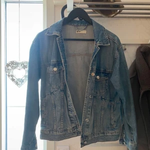 Blå jeansjacka från Gina tricot - Klassisk blå jeansjacka från Gina tricot i storlek S. Jackan har två bröstfickor med knappar, framfickor och snygga sömdetaljer. Perfekt oversized känsla och passar till allt. Tillverkad i slitstarkt jeanstyg med krage och knappstängning framtill.