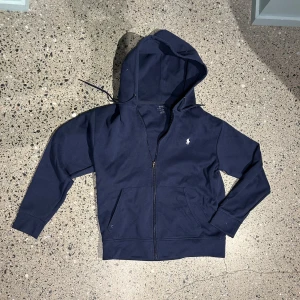 Marinblå hoodie från Polo Ralph Lauren - Säljer en marinblå hoodie från Polo Ralph Lauren med dragkedja och huva. Stroken M. Hör av dig vid frågor!