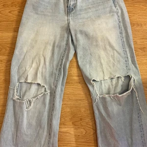 Ljusblå slitna jeans med hål vid knäna - Ljusblå jeans med rejält slitna och trasiga hål över båda knäna. Klassisk femficksmodell med raka ben och normal passform. Jeansen har en cool, avslappnad vibe och är perfekta för dig som gillar streetstyle. Materialet är klassisk denim i bomull.