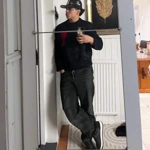  Ami Paris Hoodie - Svart stickad tröja från Ami Paris med röd hjärtlogga och bokstaven A på bröstet. Tröjan har ribbade muddar vid hals, ärmslut och nederkant. Klassisk passform och rund halsringning, perfekt för dig som gillar stilrena detaljer.