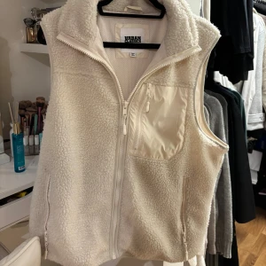 Vit fleeceväst - Mysig vit teddyväst från urban classics. Västen har en bröstficka med dragkedja samt två sidofickor med dragkedja. säljes då den va lite för oversize för min smak. strl s men passar även M och L. Nypris 699:-
