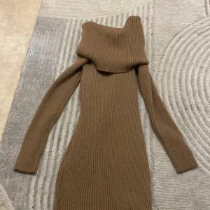 Ribbad brun stickad klänning - Snygg ribbad brun stickad klänning med lång ärm och hög krage. Klänningen har en figurnära passform och är tillverkad i ett mjukt stickat material som känns skönt mot huden. Perfekt för dig som gillar en enkel men stilren look.