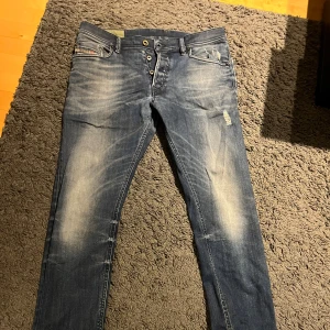 Diesel industry jeans med slitningar - Säljer ett par blå jeans från Diesel med snygga slitningar och ljusa partier framtill och baktill. Jeansen har klassisk femficksdesign, knäppning med knappar och smal passform.