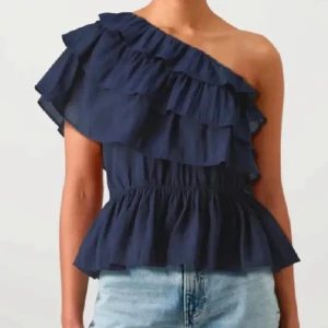 Mörkblå omlott volang topp oneshoulder - Säljer en mörkblå oneshoulder topp med breda volanger och omlott-design vet inte vart den kommer ifrån men köptes här på plick och är i bra skick förutom att den är lite skrynklig men inget som inte går att fixa. Hade inte så bra bilder så tveka inte på att fråga om fler. Storlek S men stor i storleken jag behövde göra den lite mindre med hjälp av säkerhetsnålar men har man lite större bröst funkar den nog bättre för det var vid brösten den var för stor🩷
