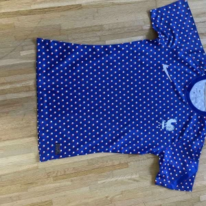 Blå prickig Nike Frankrike fotbollströja - Blå fotbollströja från Nike med vita och röda prickar över hela tyget. Tröjan har korta ärmar, rund halsringning och Frankrikes landslagsemblem på bröstet. Tillverkad i lätt och ventilerande material som passar perfekt för träning eller match.