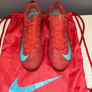 Nike Mercurial Vapor 16 elite  fotbollsskor - Säljer ett par Nike Mercurial Vapor 16 fotbollsskor i röd och turkos färg med coola detaljer. Skorna har snörning, platt sula med dobbar och är tillverkade i syntetmaterial. Perfekta för dig som vill sticka ut på planen. Skickas med originalpåse och box 