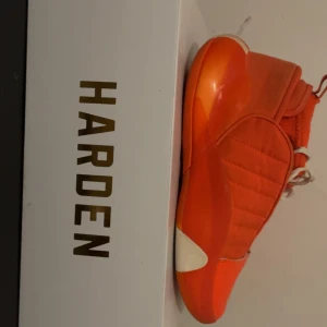 Adidas Harden Volume 7 orange sneakers - Säljer ett par Adidas Harden sneakers i en riktigt fet orange färg med vita detaljer. Skorna har snörning och en platt sula med mönstrad undersida för extra grepp. Ovandelen är tillverkad i syntet och textil, perfekt för dig som gillar basketstil och sportig vibe.