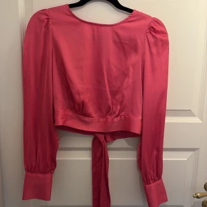 Blus - Rosa kort blus i satin med öppning och knytning i ryggen. Helt oanvänd! Storlek S men passar nog xs-m med tanke på att man knyter själv💕