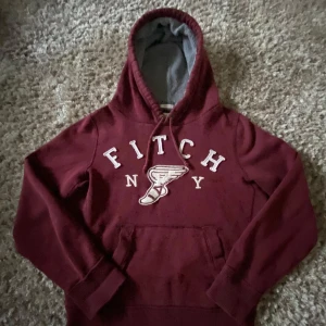 Vinröd hoodie Abercrombie & Fitch M - Snygg vinröd hoodie från Abercrombie & Fitch med broderad logga och text på bröstet. Tröjan har huva med grått foder, snörning och klassisk känguruficka. Perfekt för chill dagar och streetstyle. Har du några funderingar så är det bara att skriva. (Kan passa folk mer small).
