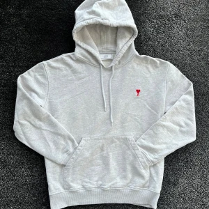 Ami paris hoodie - Säljer en ljusgrå hoodie från Ami med broderat rött hjärta och bokstaven A på bröstet. Tröjan har huva med snörning och klassisk känguruficka. Tillverkad i mjuk bomull, perfekt för chill dagar. Storlek L men passar med M, skick 8/10 finns täcken på användning. Pris går att diskutera✅