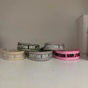 Christian Dior J'Adior armband - 199 styck går ner i pris vid bulk Säljer flera Christian Dior J'Adior armband i olika färger: beige, grå, och rosa. Armbanden har broderad text och är tillverkade i tyg med justerbar knytning. Perfekt accessoar för att lyfta din stil med en lyxig touch.
