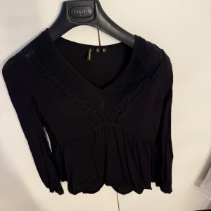 Svart blus med spetsdetaljer - Svart blus från Zalando/ Superdru med v-ringning och fina spetsdetaljer längs bröstet. Blusen har långärmade ärmar och en lätt volang nedtill. 