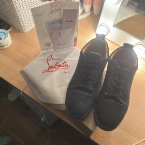 Christian Louboutin marinblåa sneakers mocka - Säljer ett par marinblåa sneakers från Christian Louboutin i lyxig mocka med ikonisk röd sula. Skorna har rund tå, snörning och diskreta broderade detaljer baktill. Insidan är fodrad i beige läder för extra komfort. Perfekta för dig som vill sticka ut med stil.
