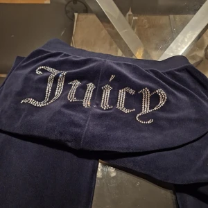 Juicy Couture mörkblå mjukisbyxor XS - Mörkblå mjukisbyxor från Juicy Couture i velour med strassdetaljer som bildar texten 'Juicy' på baksidan. Byxorna har en klassisk relaxed passform och resår i midjan. Perfekta för en chill och trendig look.
