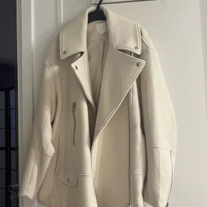 Beige HM JACKA med dragkedja - Snygg beige jacka  med bred krage och silvriga dragkedjor. Jackan har en oversized passform och coola detaljer som stora slag och fickor med lock. Perfekt för dig som vill ha en stilren och trendig look.