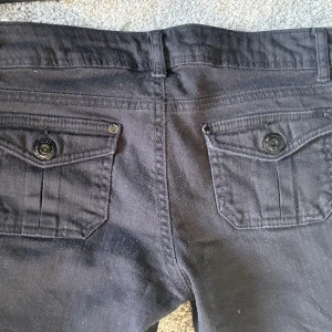Svarta super lågmidjade jeansbyxor - Svarta jeansbyxor med raka ben och snygga ficklock med knappar både fram och bak. Byxorna har bälteshällor och klassisk design, perfekta för en stilren look. Materialet är jeans och passformen är normal. (Inte skinny jeans) pris kan diskuteras!!