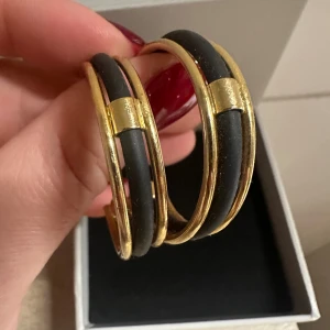 Svart och guldiga hoops örhängen - Stilrena hoops örhängen i svart och guld med cool design. De är runda och har en mix av mattsvart och glänsande guldfärg, vilket ger en modern och edgy vibe. Perfekta för att lyfta vilken outfit som helst med en touch av lyx.