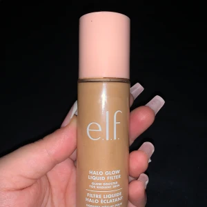 e.l.f. Halo Glow Liquid Filter - Glow booster i flytande form från e.l.f. i en beige nyans. Kommer i en smidig flaska med ljusrosa lock och ger huden en strålande finish. Perfekt för dig som vill ha en naturlig glow och jämnare hudton.