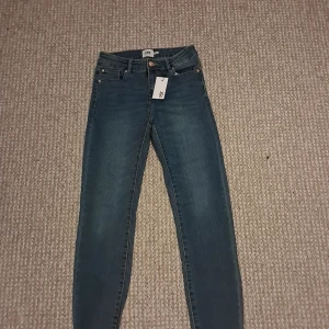 Blå skinny jeans från 157, strl 160 - Snygga blå jeans från 157 i modellen Skippy. Jeansen har klassisk femficksdesign, skinny passform och normal midja. Tillverkade i stretchig denim för en bekväm känsla. Perfekta för dig som gillar en smal siluett och enkel stil.