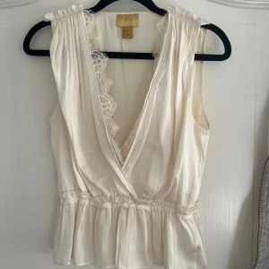 Vit omlottopp med spets från H&M - Söt vit omlottopp i silke från H&M i storlek 32. Toppen har djup v-ringning med spetsdetaljer längs kanten, ärmlös och ett rynkat midjeparti! Passar en storlek 34! 