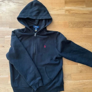 Svart hoodie från Ralph Lauren - Säljer en klassisk svart hoodie från Ralph Lauren med dragkedja. Passar storlek 160. Den är i mycket bra skick.