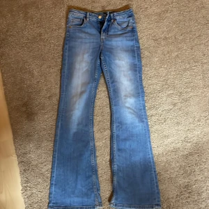 Blå bootcut jeans  - Snygga blå jeans från Kappahl i storlek 152. Jeansen har klassisk femficksdesign, bootcut-ben och ljus tvätt med lätt slitning framtill. Perfekta för dig som gillar en retroinspirerad look med utsvängda ben.
