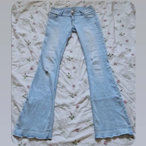 Lågmidjade Ljusblå bootcut jeans  - Jätte fina ljusblåa lågmidjade bootcut jeans med snygga detaljer!❤️ Dom är i bra skick, har dock sprättat upp dom längst ner, och så finns det två små hål som ni ser på sista bilden, men som knappt syns när man har på sig dom🫶💗 Mått: midjemått 36cm(dom är däremot väldigt stretchiga), innerbenslängd 82cm. Pris kan diskuteras, hör av er vid frågor!🤗