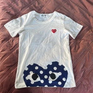 Vit Cdg t-shirt  - Säljer en vit t-shirt från Comme des Garçons Play i storlek S. Framsidan har det ikoniska röda hjärtat med ögon på bröstet och ett stort blått hjärta med vita prickar och ögon nedtill. T-shirten är i mjuk bomull och har rund hals och korta ärmar. Är liten i storleken. Helt ny och i Suveränt skick 10/10