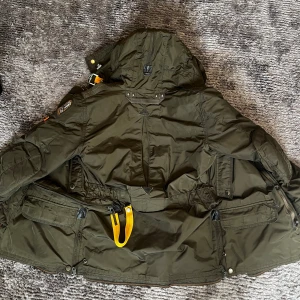 Parajumpers grön parkajacka Small - Säljer en grön parkajacka från Parajumpers, modell Masterpiece Series Anthology. Jackan har huva, flera fickor, gul remdetalj och insida med mjuk fuskpäls. Köpt på NK för ca 7000. Pris kan diskuteras.