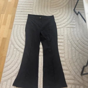 Svarta bootcut kostymbyxor - Svarta kostymbyxor med bootcut-silhuett och klassisk knappstängning. Byxorna har en snygg, utsvängd passform och är perfekta för en stilren look. Materialet känns mjukt och följsamt, och midjan är normalhög.