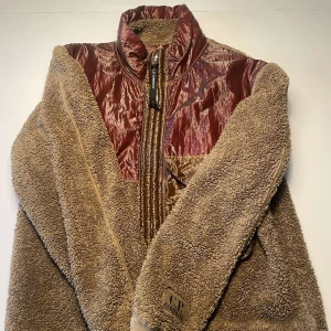 Brun teddyjacka från C.P. Company - Säljer en brun teddyjacka från C.P. Company med glansiga vinröda paneler upptill. Den är i bra skick och är perfekt nu till höst. Den är bra tätt och därför blir varm och väldigt skön. Det är i storlek M. Mitt pris ligger på 600. 