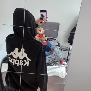 Svart hoodie från kappa - Svart hoodie från kappa. Fint skick, dock har plastbitarna som ska sitta längst ner på snörena lossnat (kolla sista bilden).