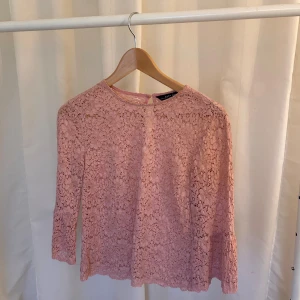 Rosa spetsblus från Zara Woman - Supersöt ljusrosa blus från Zara Woman i spets med blommigt mönster. Blusen har trekvartsärm och rund halsringning, samt en liten knapp i nacken. Perfekt för dig som gillar romantisk och feminin stil.