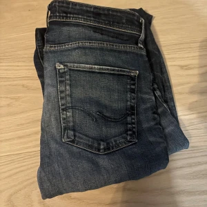 Mörkblåa jeans Jack & Jones - Snygga mörkblå jeans från Jack & Jones med slitningar och skinny fit. Klassisk femficksmodell med coola detaljer och lätt tvättad look. Perfekta för dig som gillar en smal siluett och streetkänsla.