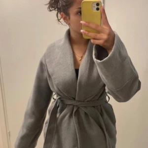 Grå omlottkappa med bälte - Säljer min Snygga gråa  kappa med bred krage och knytbälte i midjan som jag totalt använd 3 gånger för mig tycker jag att den jätte fin och sitter så bra de storlek s/xs skriv gärna fler bilder inga skador alls!💕