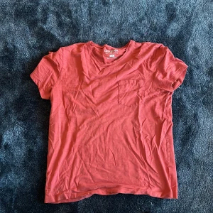 Röd t-shirt från Dobber med ficka - Snygg röd t-shirt från Dobber i storlek M. T-shirten har en klassisk rund hals, korta ärmar och en liten bröstficka. Tillverkad i mjuk bomull som känns skön mot huden. Perfekt för dig som gillar enkel och stilren design.